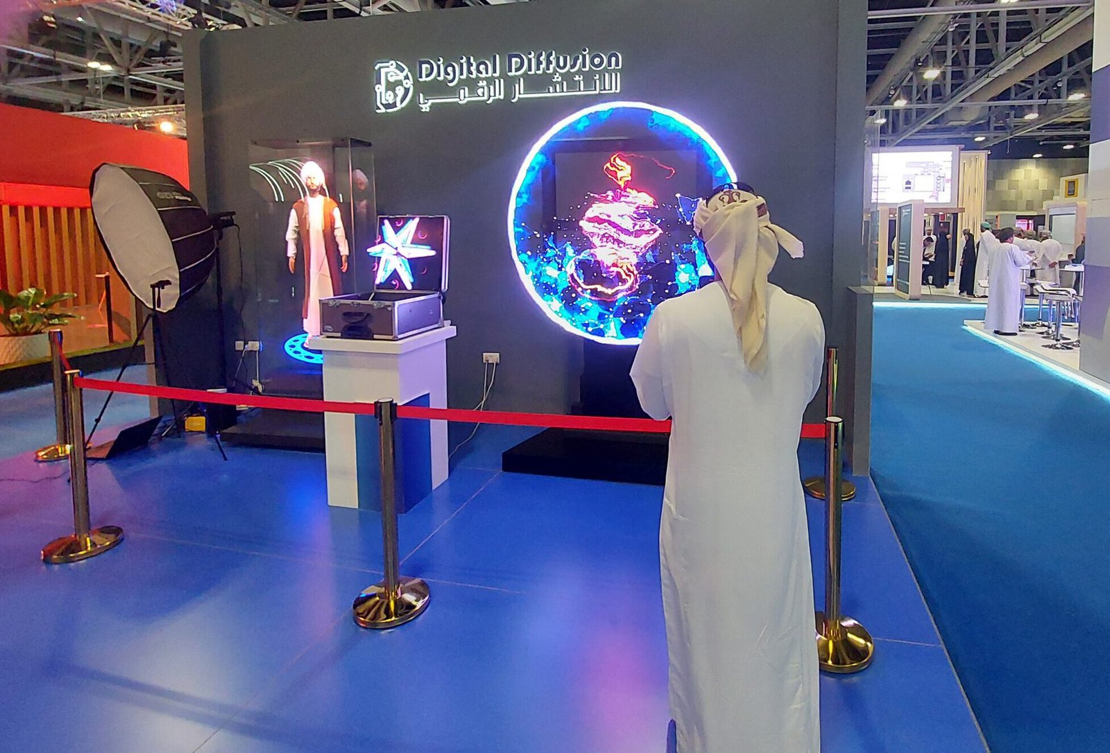 An Omani visitor in traditional attire views a vibrant holographic solution at Digital Diffusion's booth at COMEX 2023, showcasing cutting-edge 3D holographic and AI technologies